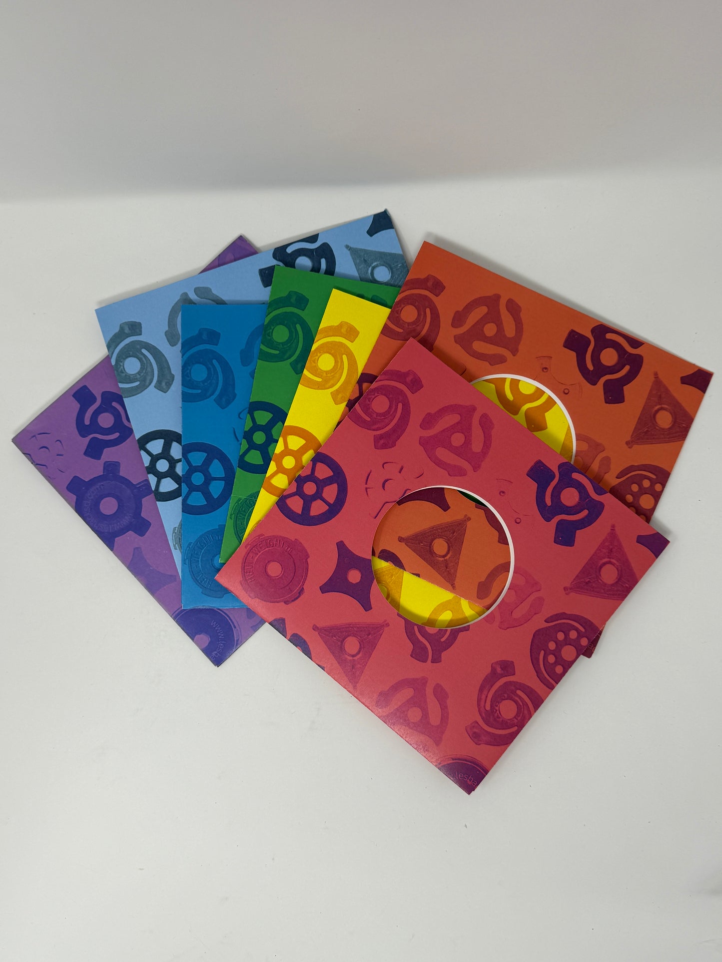 The picture shows a set of seven inch record sleeves in a rainbow color array representing ROYGBIV. The sleeves are designed with an array of images of vintage record adapters.